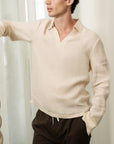Man wearing a beige sweater and dark pants against a neutral background