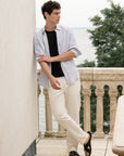 Man in light shirt and white pants standing on a balcony with trees in the background