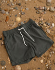 Black shorts with a white drawstring on a sandy background with small rocks and pebbles.