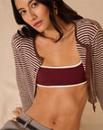 Woman wearing a maroon bikini top with a striped cover-up on a beige background
