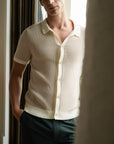 Man wearing a light-colored short-sleeve shirt and dark pants indoors.