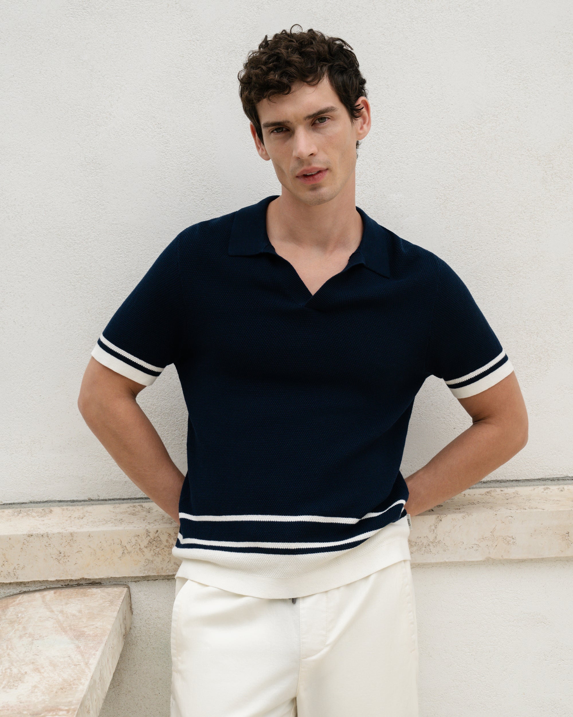 Man wearing a navy polo shirt with white trim against a light background