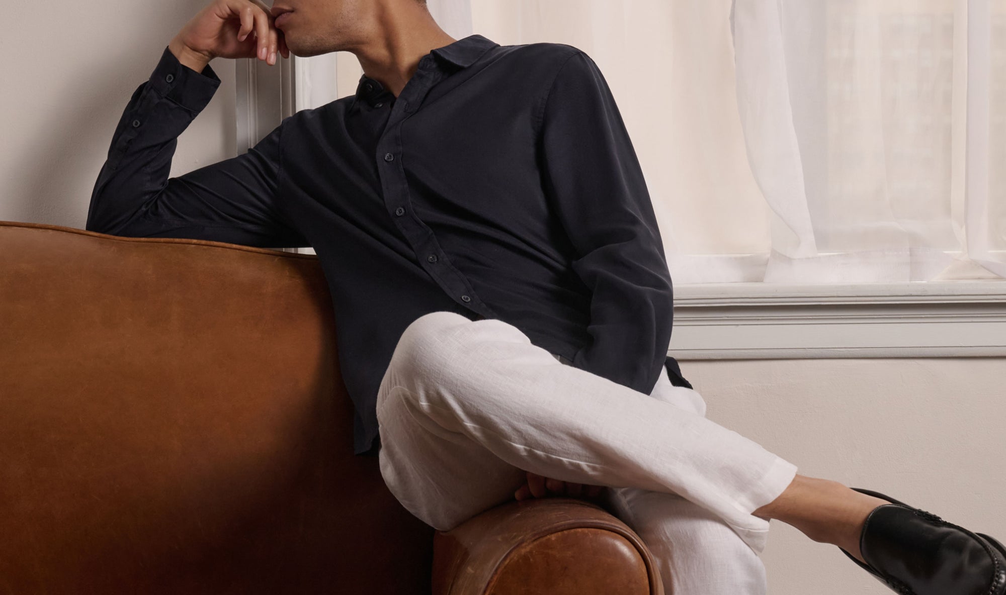Person sitting on a brown leather chair wearing a dark shirt and white pants.