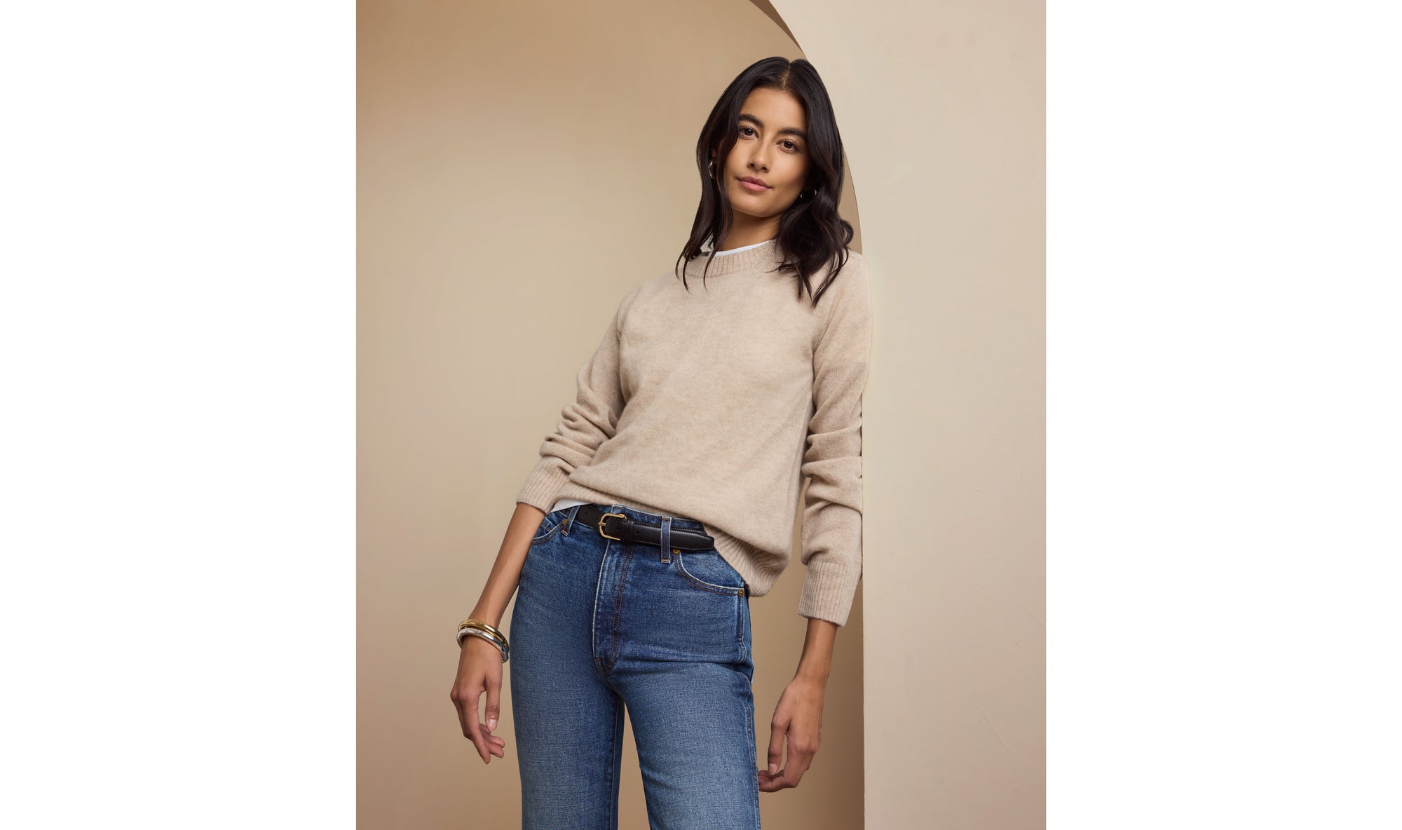 Woman wearing a beige sweater and blue jeans against a beige background