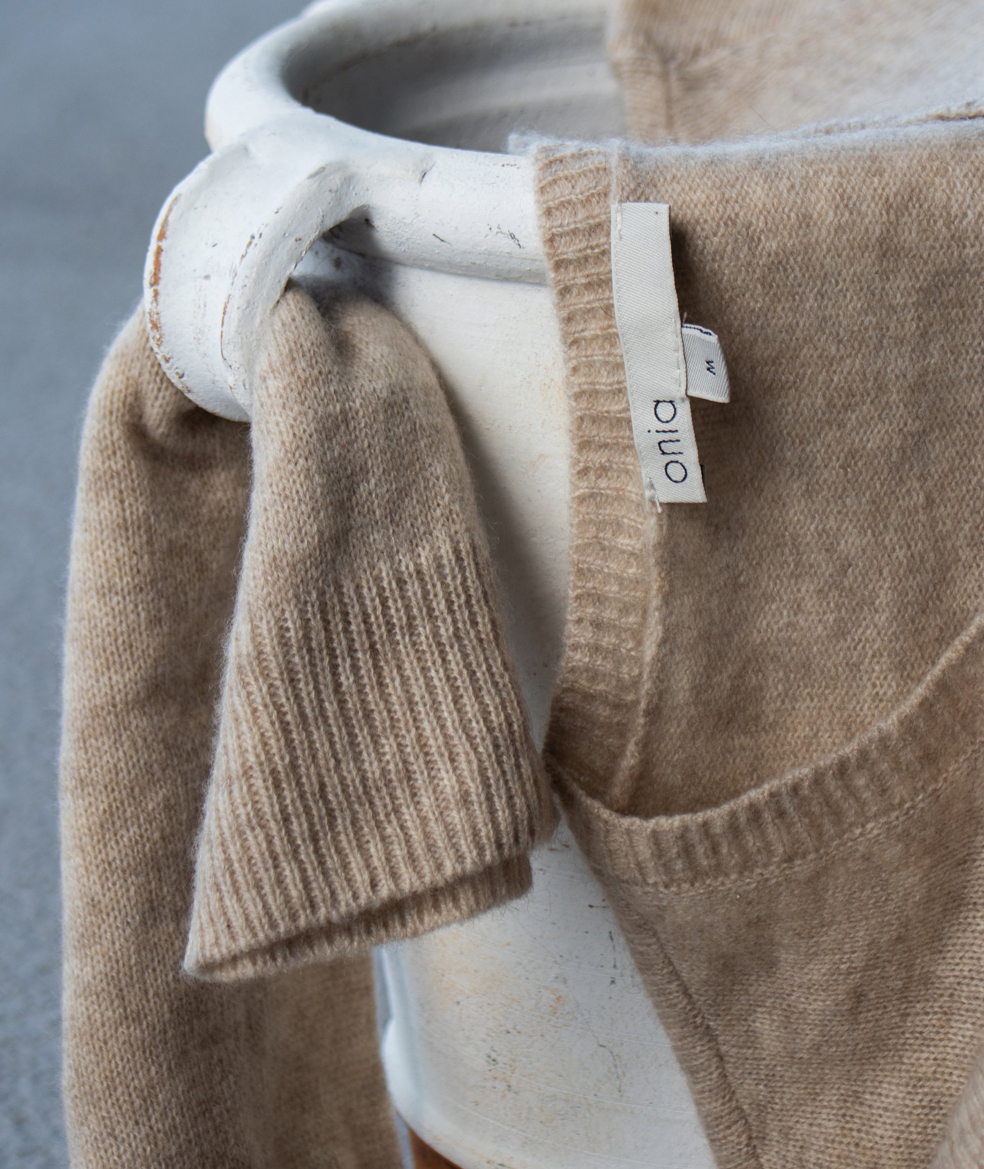 Close-up of a brown knitted cashmere sweater with a visible brand tag on a neutral background