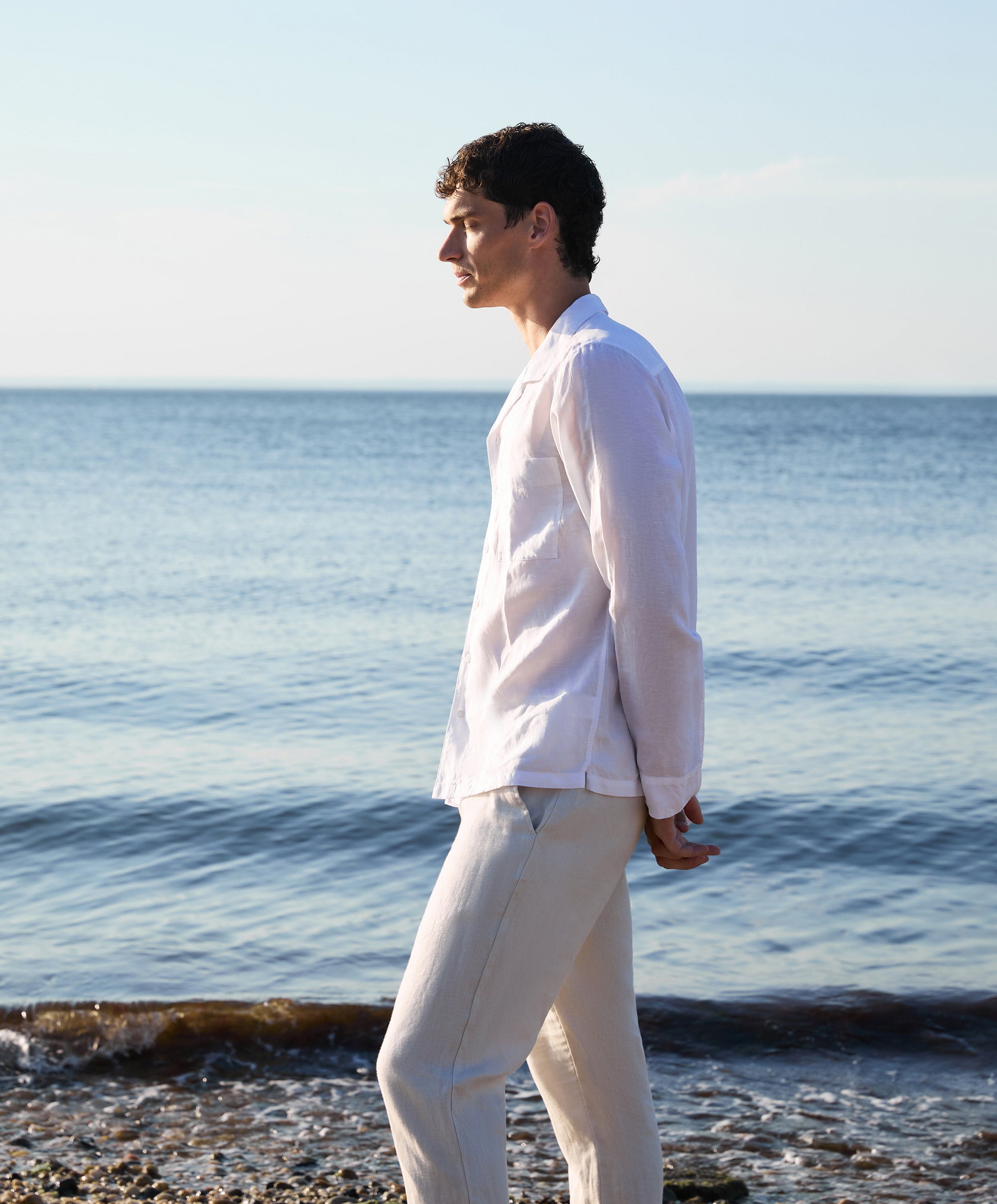 Man in a white shirt and beige pants standing on a beach with ocean in the background