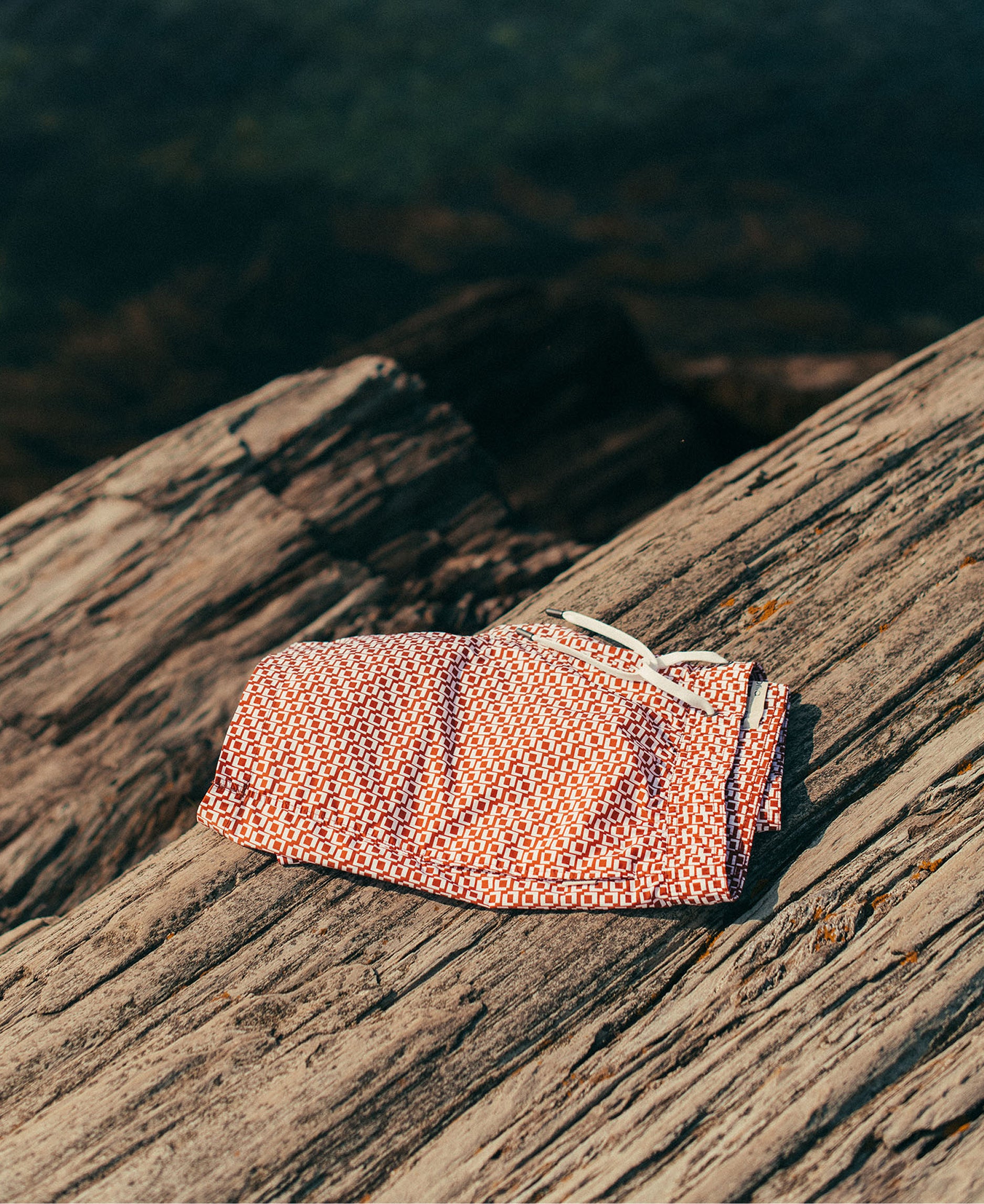 Folded pink swim trunk on a wooden surface with a blurred natural background