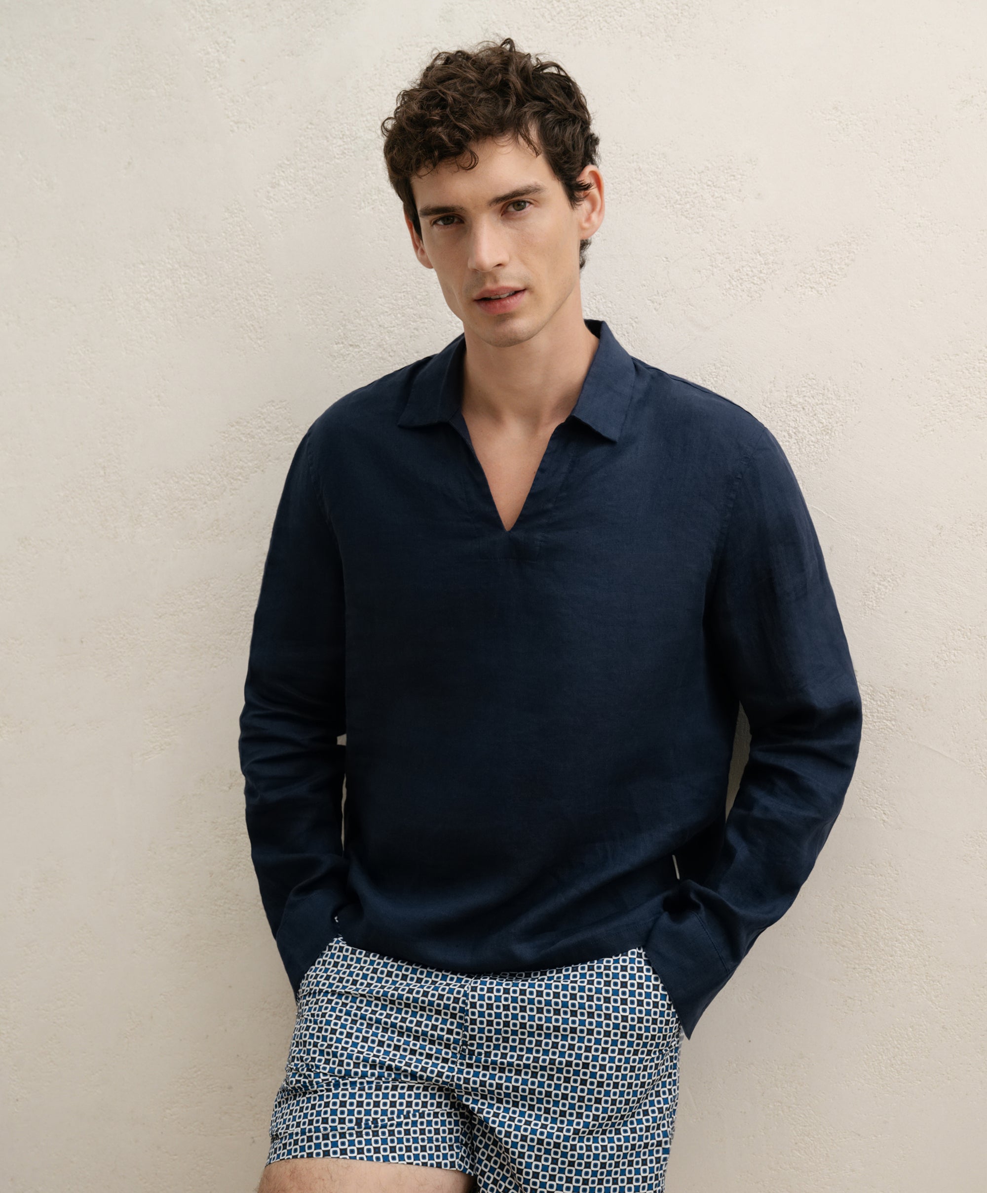 Man wearing a navy long-sleeve shirt and patterned shorts against a beige background