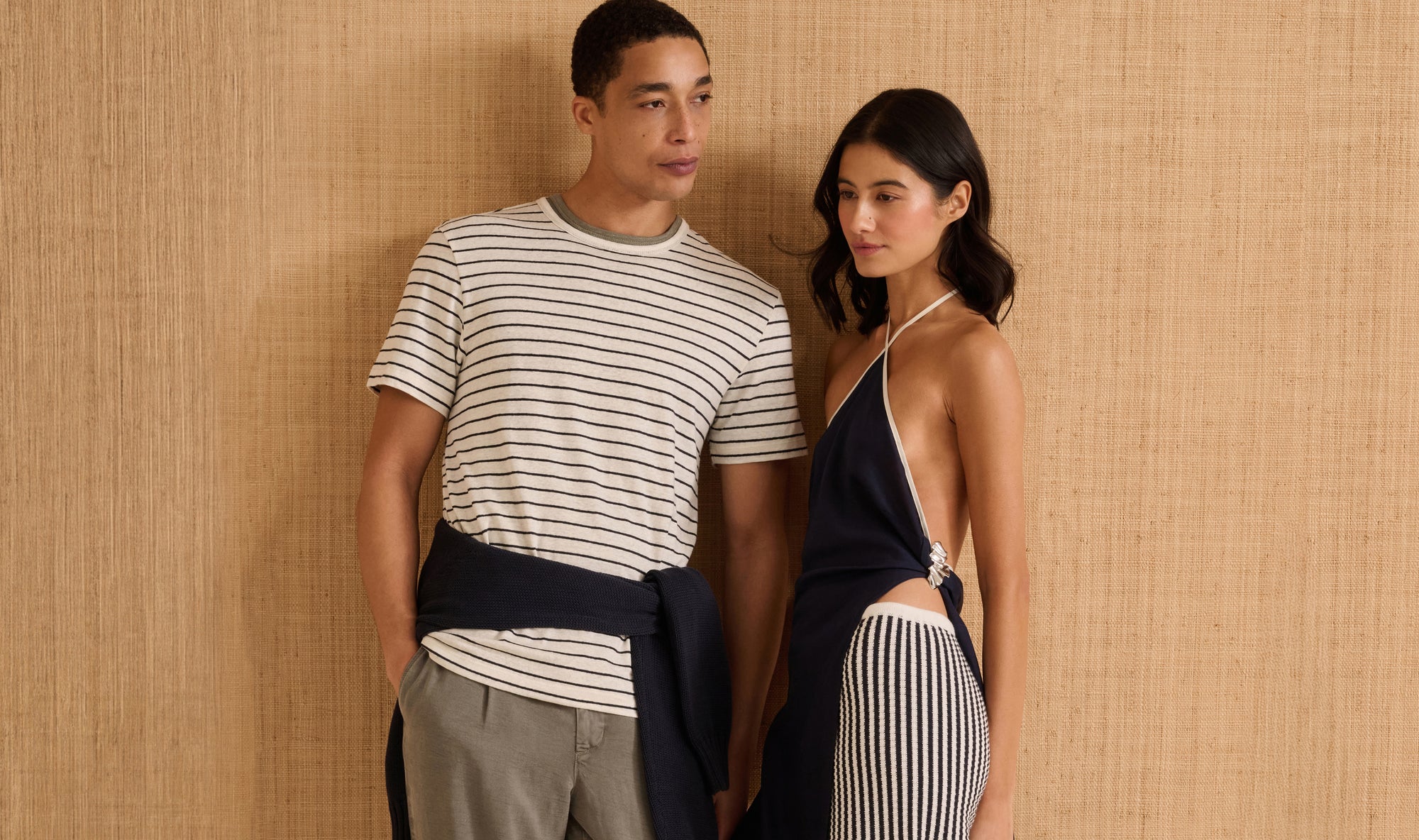 Man and woman standing together against a beige wall, wearing striped and navy outfits.
