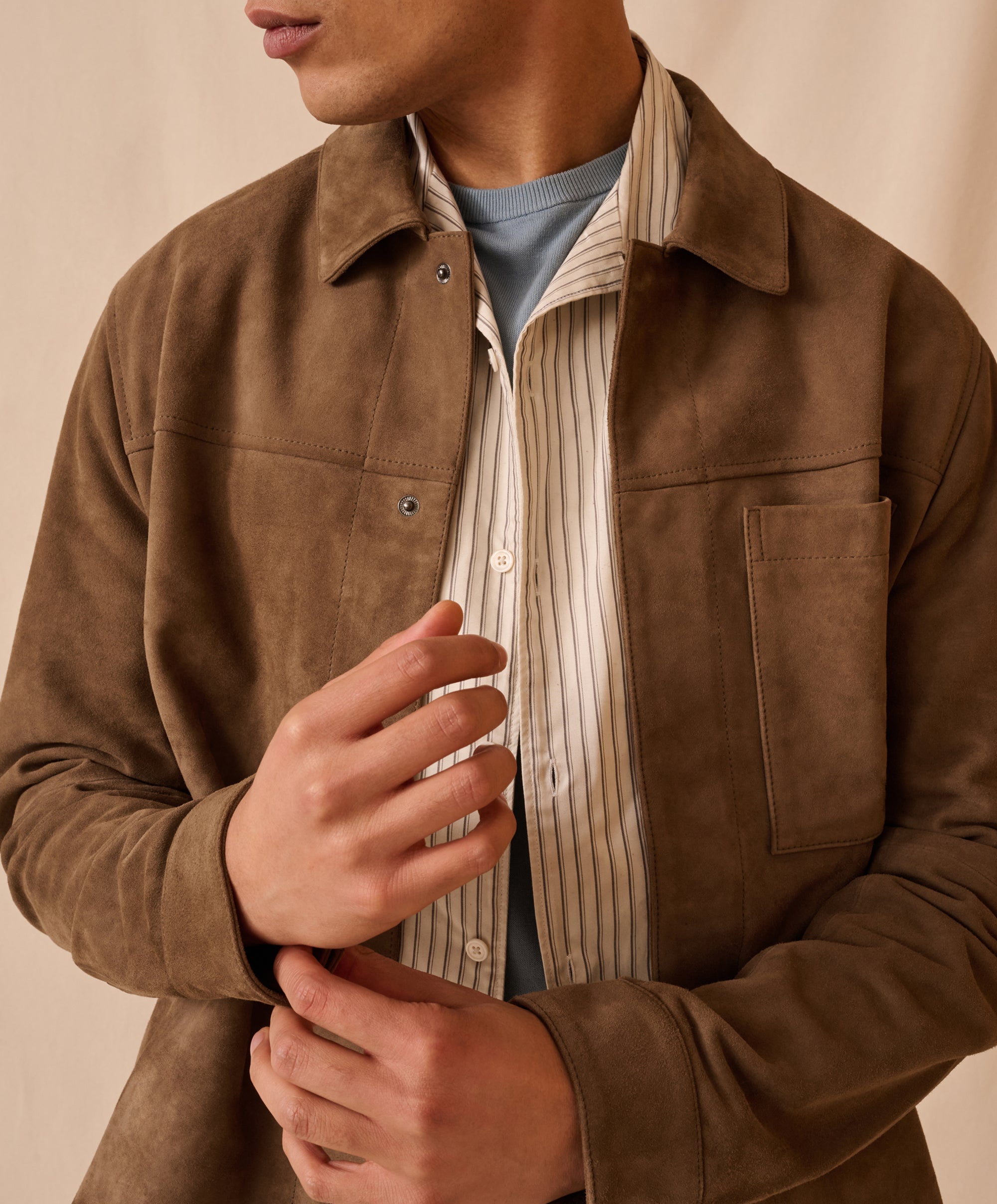 Man wearing a brown Onia suede jacket over a striped shirt on a beige background