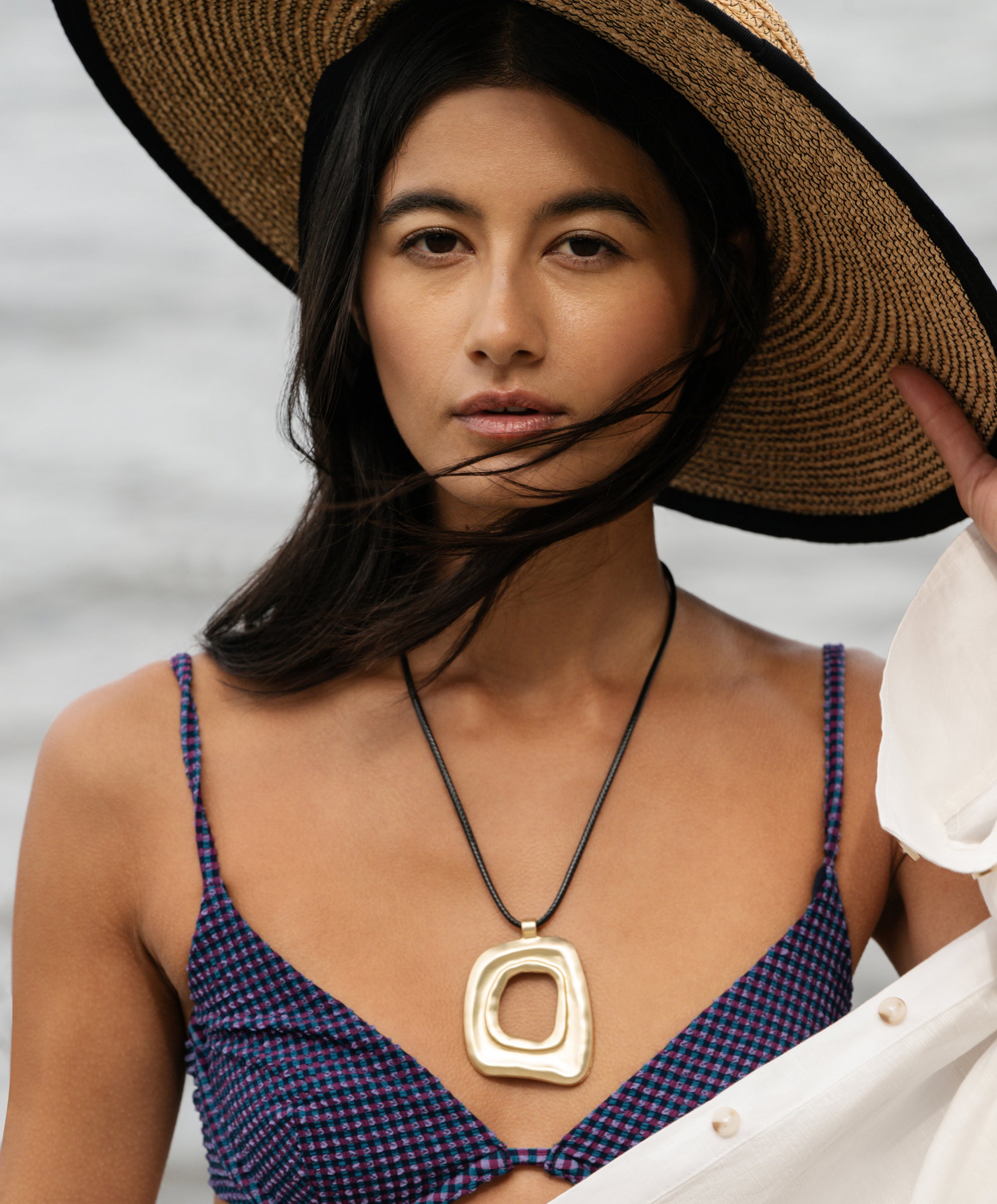Woman wearing a straw hat and a necklace with a gold pendant against a neutral background
