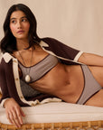 Woman wearing a brown and white knit cardigan over a striped bikini on a beige background