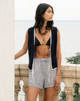 Woman wearing a black bikini top and striped shorts with a navy cover-up in an outdoor setting.