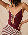 Maroon soleil one piece with white trim worn by a woman on a beige background