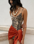 Woman wearing a leopard print top and orange skirt against a light background