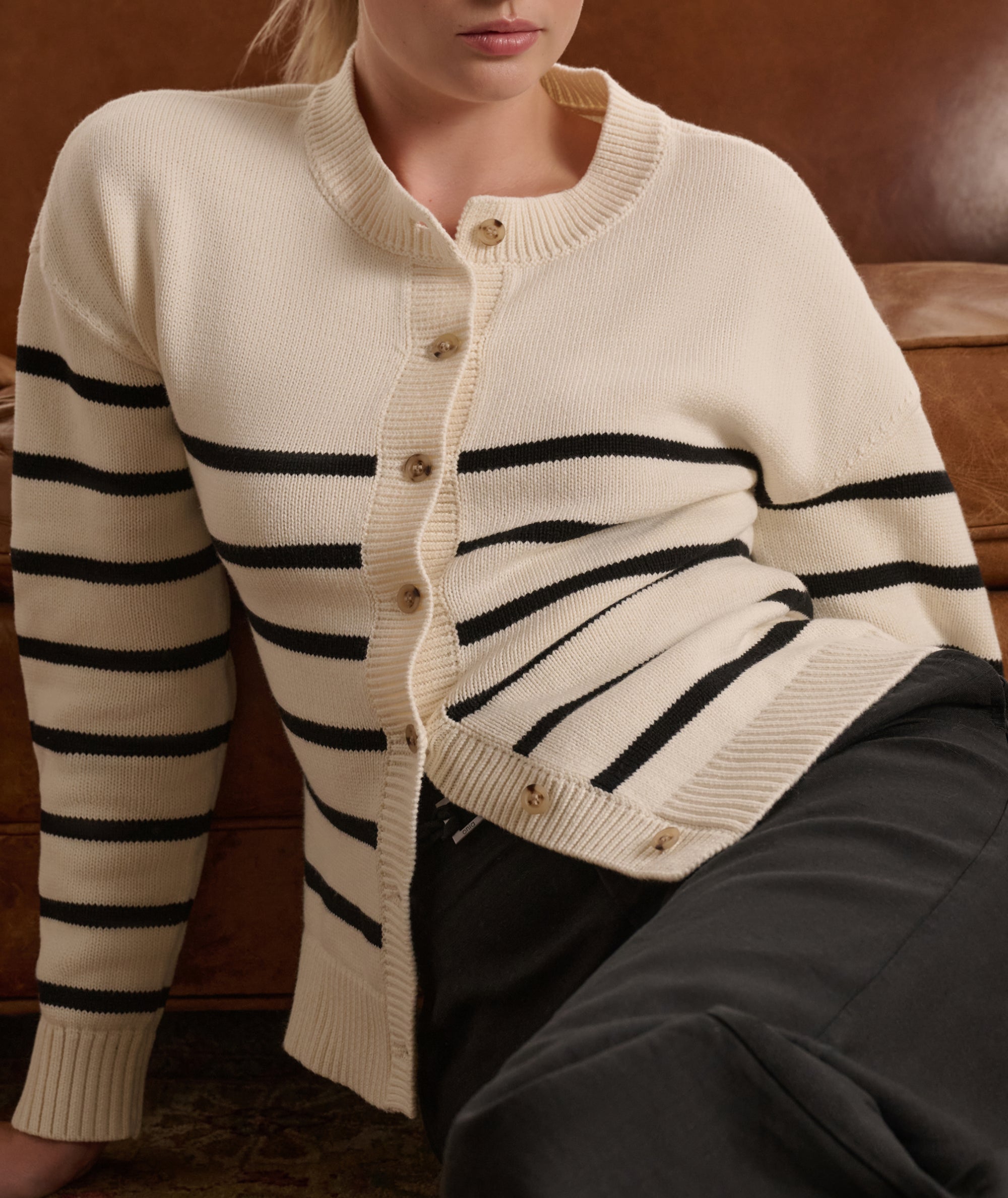 Person wearing a cream cardigan with black stripes sitting on a brown couch.