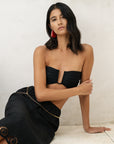 Woman wearing a black strapless top and black skirt with gold accents against a neutral background